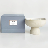 A large, off-white ceramic Spiritual Candle by Blueme, made with a soy wax blend and five wicks, sits next to a light blue BUEME SPIRITUAL box, evoking calming wellness on a simple, light background.