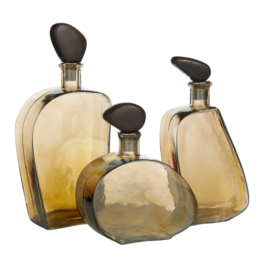 Three amber-colored Calhoun Decanters by Arteriors, featuring hammered glass and bronze-plated brass stoppers, are grouped together on a plain white background.