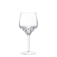 A clear Folia Stemware wine glass by Saint-Louis features a hand-cut, faceted base that tapers to a smooth stem and flat circular base, displayed against a white background.