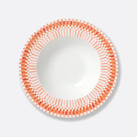 A white Terra Rosa Dinnerware bowl by Bernardaud, featuring an orange and pink geometric rim of rectangles and lines, is shown from above on a light gray background. Made in Limoges, France.