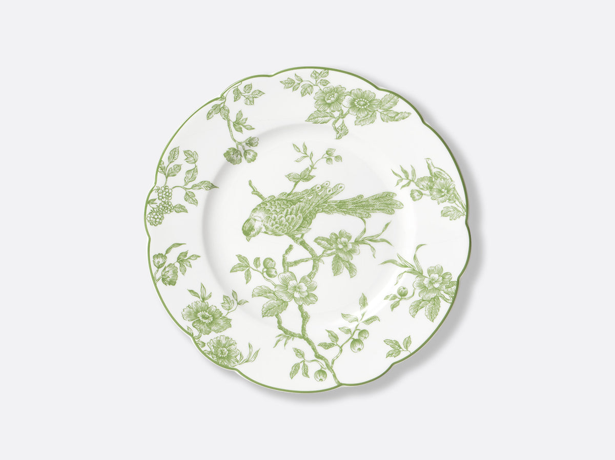 Bernardaud’s Albertine Dinnerware is a white ceramic plate with scalloped edges, adorned with a green floral and bird motif inspired by toiles de Jouy, featuring a perched bird among flowers and leaves on the rim and center.
