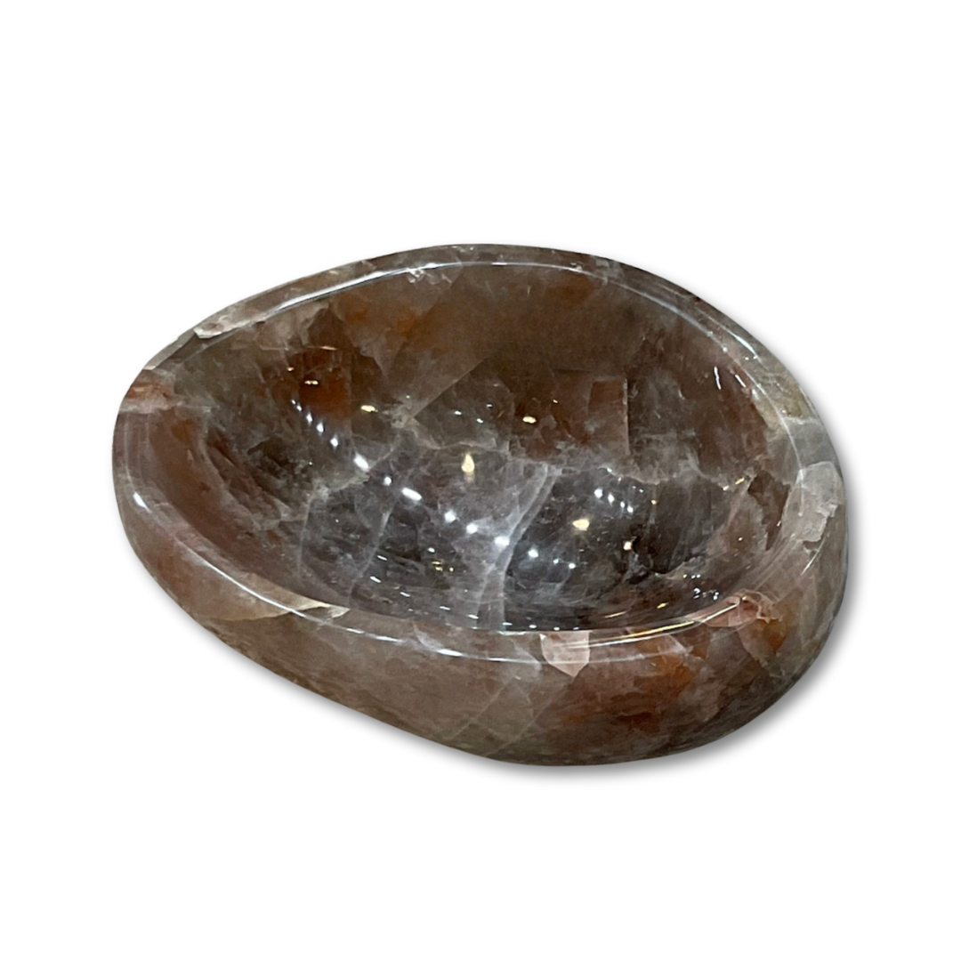 The Verona Prive Agate Quartz Bowl features a polished, oval shape with a faceted surface in rich brown tones. Its glossy texture and light reflections make it a striking decorative piece for any setting.