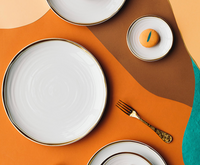 A flat lay of Bernardaud's Albatre Dinnerware - Gold, featuring gold-rimmed plates, a gold fork, and a small plate with an orange cookie on an abstract backdrop in orange, brown, teal, and beige exudes effortless wabi-sabi elegance.
