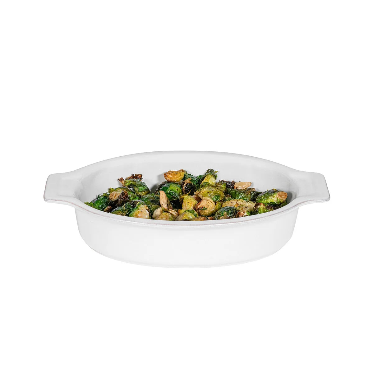 A Juliska Puro Oval Baker Whitewash 12″ filled with roasted Brussels sprouts and mushrooms, presented against a plain white background for an elegant oven-to-table display.