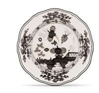 The Oriente Italiano Albus dinnerware by Ginori 1735 is an Italian porcelain plate with a scalloped edge, decorated in black floral patterns and a landscape on white, featuring flowers, leaves, and a building inspired by Ginori Oriente.