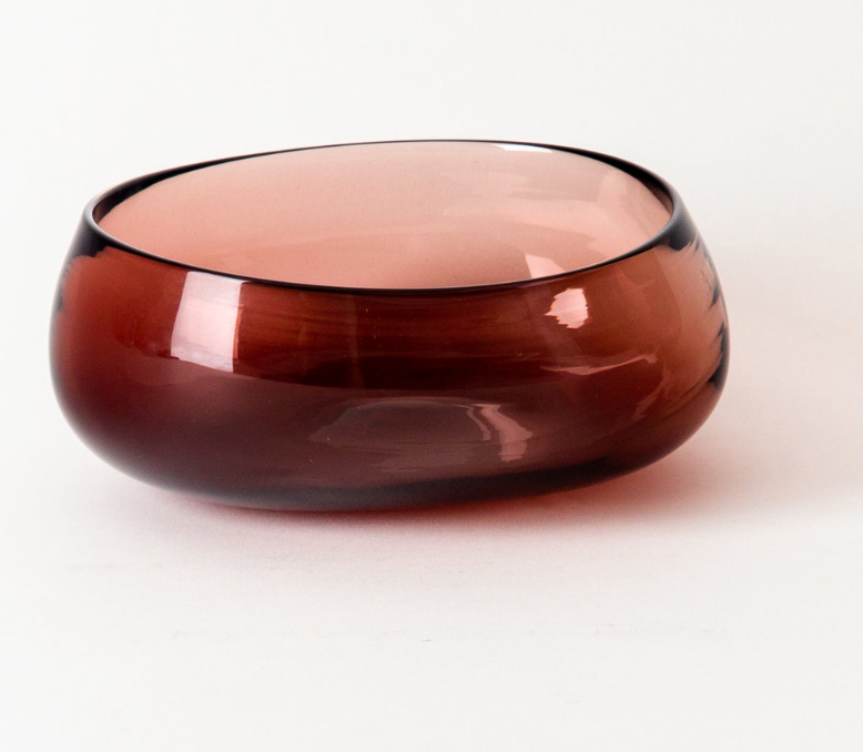 The Nesting Bowls Rose by Gary Bodker is a hand-blown glass bowl with smooth, uneven edges and a glossy deep reddish-brown finish, shown against a plain white background.