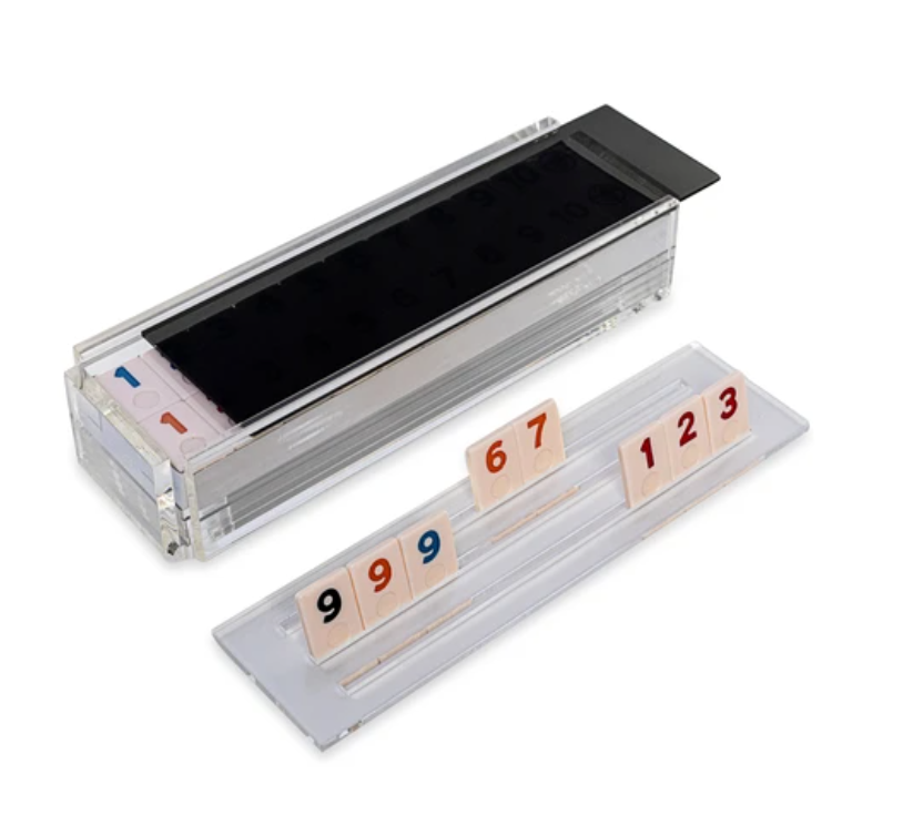 The Luxe Dominoes Rummy Acrylic Game Set features clear numbered tiles in holders displaying “9 9 9 6 7” and “1 2 3.” With a sliding cover and organized slots, it’s the perfect gift for rummikub lovers.
