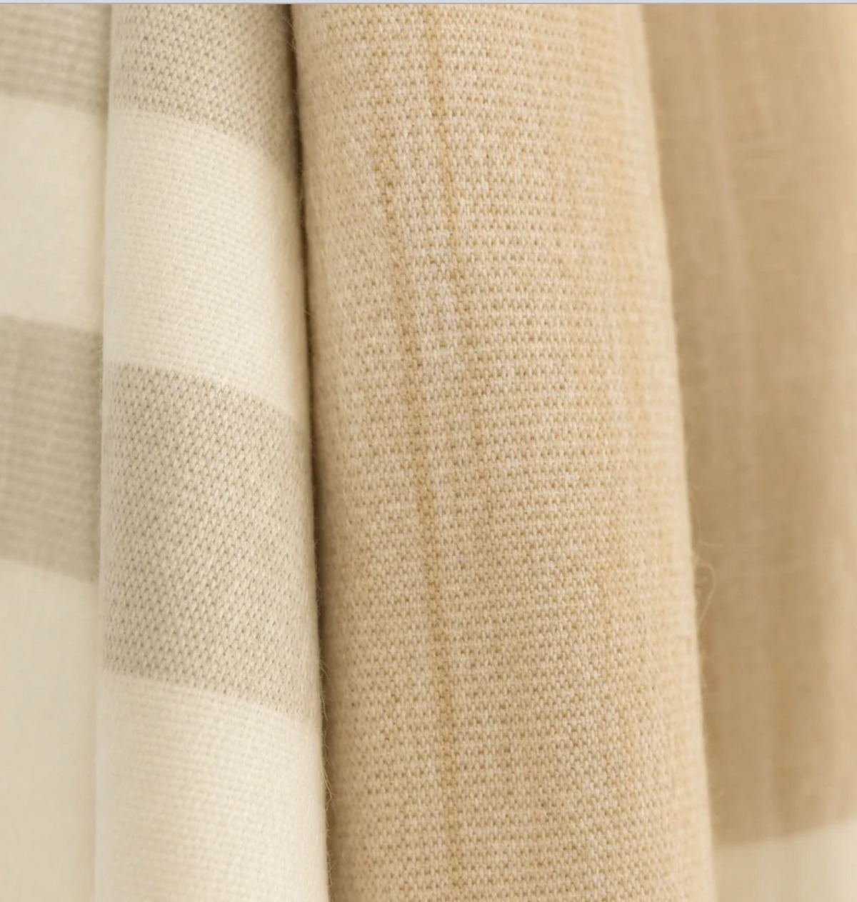 Close-up of the Purple Nest Kallpa Collection Alpaca Throw in Tobacco & Wheat, featuring folded fabric with a neutral-toned striped pattern and a solid tan textured weave.
