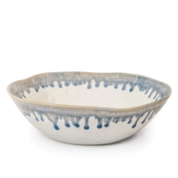 The Simon Pearce Burlington Dinnerware Pool handmade ceramic bowl features an uneven rim, white glaze with a blue drip pattern—an eye-catching, unique piece to enhance your Burlington dinnerware collection.