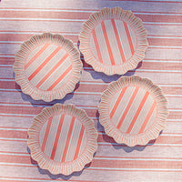 Four Juliska Cabana Stripe Melamine Dinner Plates in coral, featuring pink and white diagonal stripes with ruffled edges, are displayed on a matching striped tablecloth for a coordinated look. Set includes 4 plates.