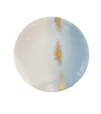 The Marie Daâge Horizon Gold Dinnerware by Marie Daâge features a round ceramic plate with a cream and light blue gradient, accented by two vertical metallic gold lines. Inspired by French tableware, it brings elegance to any setting. Shown on a plain white background.