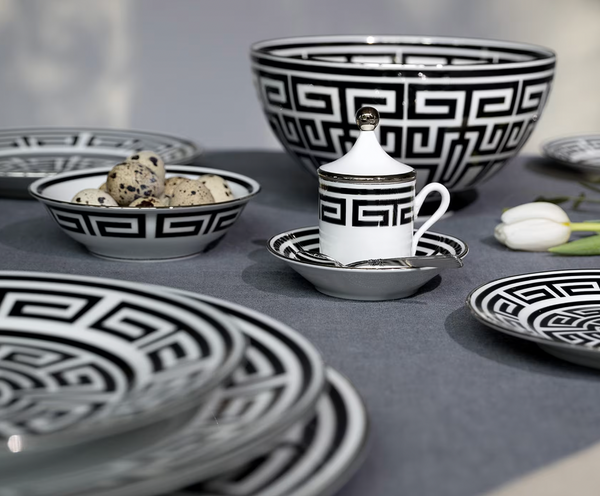 A table set with Ginori 1735’s Labirinto Dinnerware Nero—black and white geometric plates, bowls, and a lidded cup—plus quail eggs and a white tulip on gray linen exudes refined elegance.