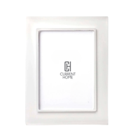 The Prisma Frame Snow White by Bella Moulding features a raised border, white insert with the Current Home logo, and UV-filtering glass for added photo protection.