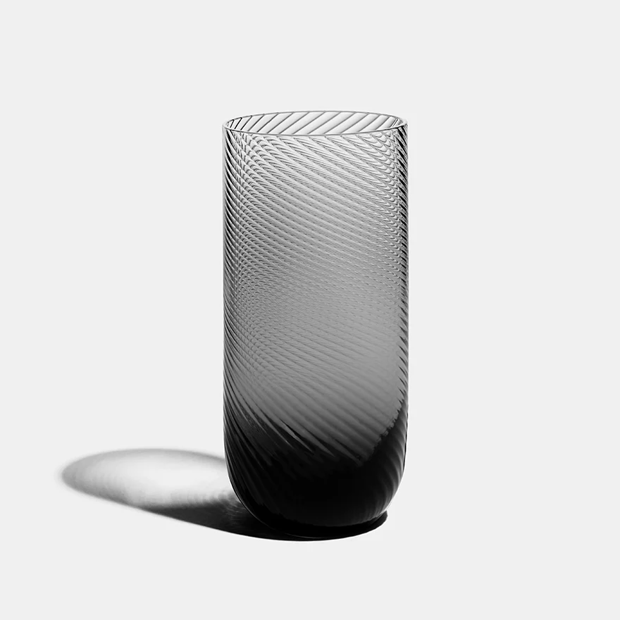 The Optic Glassware Smoke Set of 2 by Richard Brendon features tall, cylindrical glasses with a textured diagonal swirl, fading from clear to dark, displayed on a light gray surface casting a soft shadow.