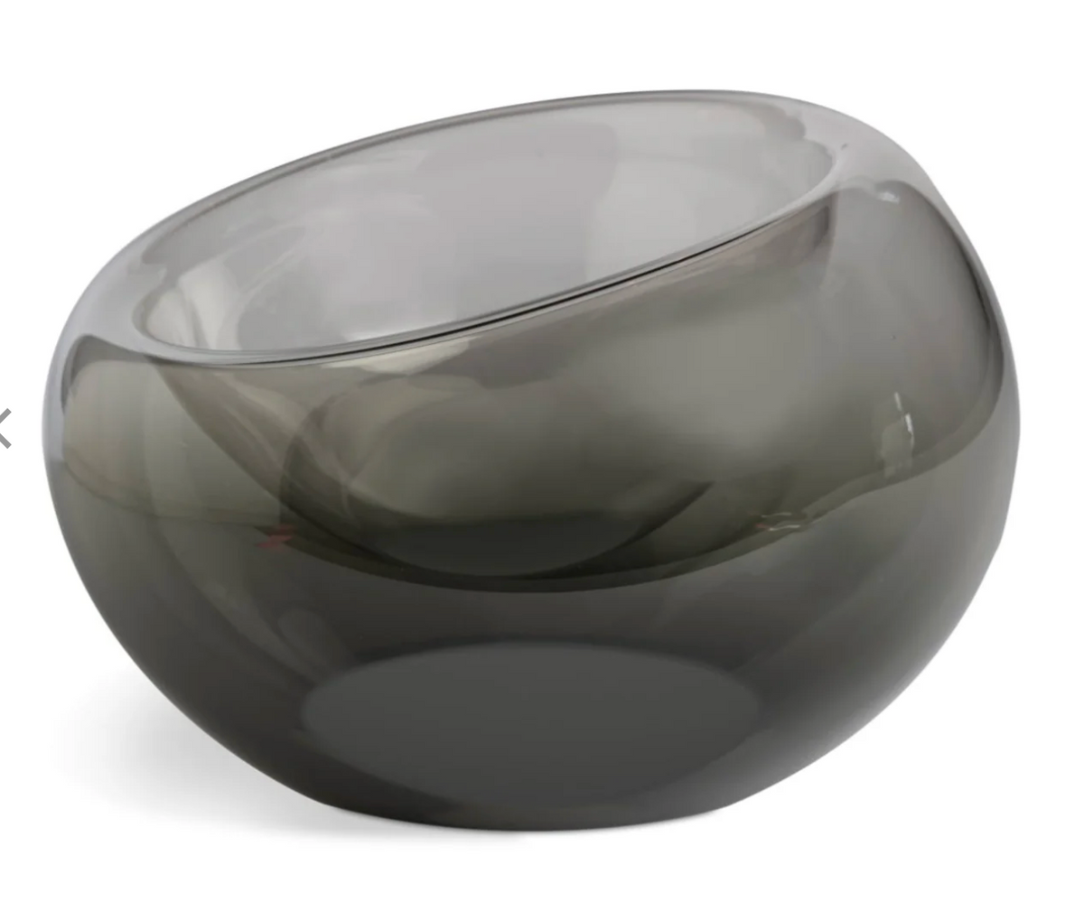 The Axiom Glass Caldera Vessel Medium 9" is a round, transparent gray hand-blown glass piece with a smooth, glossy finish and an asymmetrical tilted rim, shown against a white background.