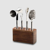 The Mary Jurek Cosmo Bar 4 pc Set On Wood Base includes a jigger, stirrer, spoon, and strainer on a sleek wooden stand—handmade stainless steel tools perfect for elevating any home bar.