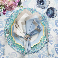 Elegant table setting featuring a blue and white patterned tablecloth, shimmery blue charger, light blue plate with gold trim, white and light blue napkin adorned with the Kim Seybert Flutter Napkin Ring Set of 4 in Lilac & Periwinkle, plus silverware.