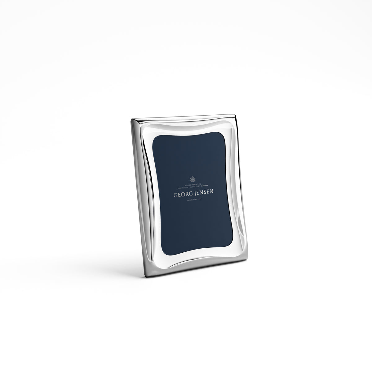The Cobra Stainless Picture Frame by Georg Jensen features a modern wavy border design and stands upright; its interior displays "Georg Jensen" in white text on a navy blue background.