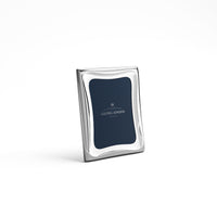 The Cobra Stainless Picture Frame by Georg Jensen features a modern wavy border design and stands upright; its interior displays "Georg Jensen" in white text on a navy blue background.