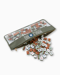 An Oh My Mahjong Tile Bag in green, featuring a clear top and "MAHJONG" label, sits open with mahjong tiles spilling onto a white surface.