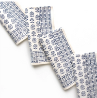 The Elise Napkin Set of 4 by Pomegranate features a blue floral and geometric pattern on white, displayed in a zigzag layout beside layered blue tableware on a white surface.