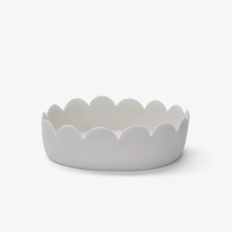 A white, oval-shaped ceramic Fleur Bowl by Tina Frey, featuring scalloped edges, is displayed against a plain white background.