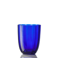 The Idra Tumbler Optic by Nason Moretti, crafted from translucent deep blue glass, stands upright on a reflective white surface against a plain white background.