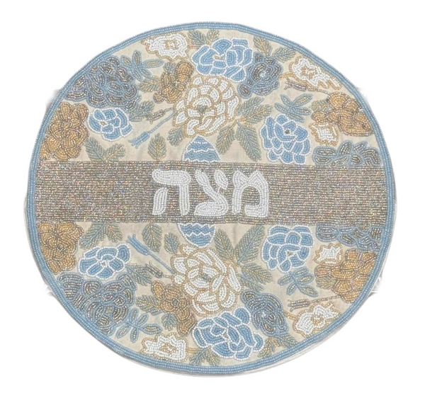 Add elegance to your Passover table with the Lyss & Kat Hebrew Floral Beaded Matzah Cover - Pastel, featuring round hand-beading, pastel blue, gold, and white floral accents, plus מצה (matzah) in Hebrew at the center.
