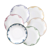 Six Marie Daâge Iris 2 ceramic plates by Marie Daâge, featuring white centers and colorful, jagged-edged borders in blue, purple, yellow, green, and pink, are arranged in an overlapping circle on a white background.