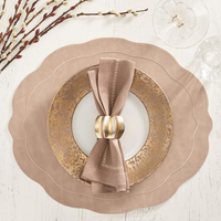 A table is set with a Kim Seybert Tailored Placemat Taupe, gold-patterned plate, white plate, mauve napkin in a gold napkin ring, plus a glass and pussy willow branches on a white wooden table.