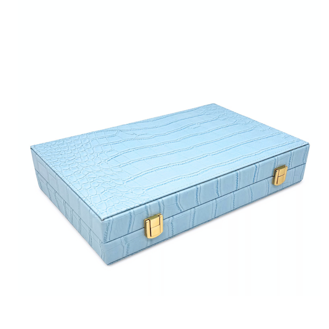 The Nile Travel Backgammon by Tizo is a light blue, crocodile-patterned rectangular compact set with gold clasps, shown closed on a white background.