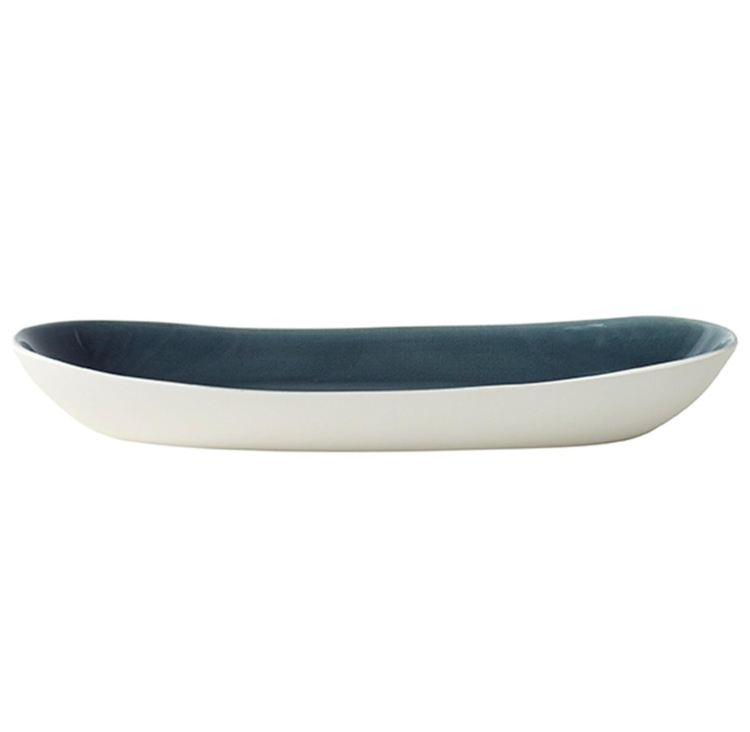 The Maguelone Outremer Dark Blue serving platter by Jars - Rosenthal features an oval shape and Mediterranean-inspired design with a white exterior and dark blue interior. Shown from the side on a plain white background. Dishwasher safe for easy care.