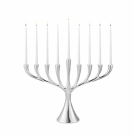 The Georg Jensen Cobra Stainless Steel Menorah displays nine lit white candles in a modern Scandinavian design, set against a plain white background.