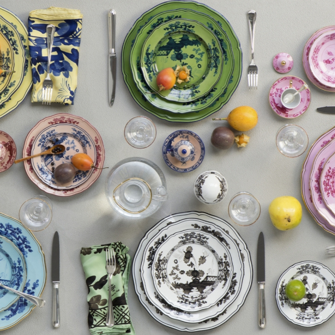 A vibrant table setting features Ginori 1735 Oriente Italiano Dinnerware Albus—handcrafted porcelain plates, bowls, and cups—paired with silverware, patterned napkins, glasses, fruits, and a light tablecloth.