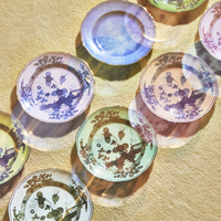 Ginori 1735 Oriente Italiano Dinnerware Albus plates with floral and bird patterns are arranged on beige, illuminated by sunlight that casts colorful, translucent reflections across the porcelain.