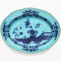 The Oriente Italiano Dinnerware Iris by Ginori 1735 is an oval Italian porcelain platter featuring a turquoise background, dark blue chinoiserie floral and landscape patterns, and a slim gold rim.