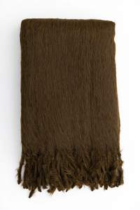 The Woolly Mammoth Throw by Dove & Donkey, a folded brown suri alpaca blanket with a fringed edge, is shown on a white background highlighting its silky soft texture.