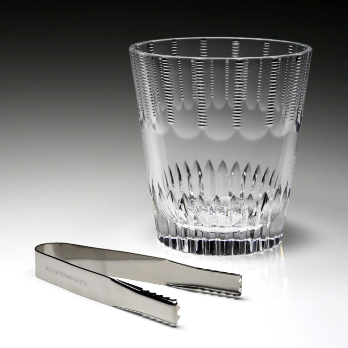 The Karen Ice Bucket by William Yeoward features a crystal design with vertical cuts and includes silver ice tongs engraved with the brand—an elegant accessory to enhance your bar setup.