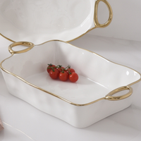 The PAMPA BAY Golden Handle Rectangle Baking Dish, made of white porcelain with gold handles and trim, holds a small cluster of red cherry tomatoes on a white marble surface.