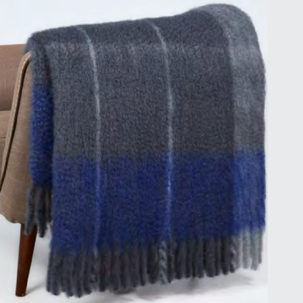 The Mantas Ezcaray Twist Frame Throw, a fuzzy mohair blanket handcrafted in Spain with blue and gray plaid and fringed edges, is draped over a brown chair.