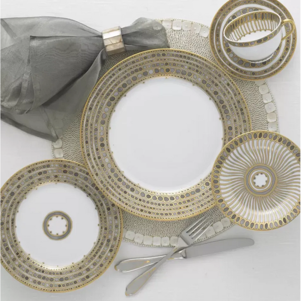 Elegant table setting with Haviland & Parlon Syracuse Dinnerware in taupe, featuring intricate gold and silver designs, a matching teacup and saucer, silverware, gray cloth napkin with silver ring, and a textured placemat.