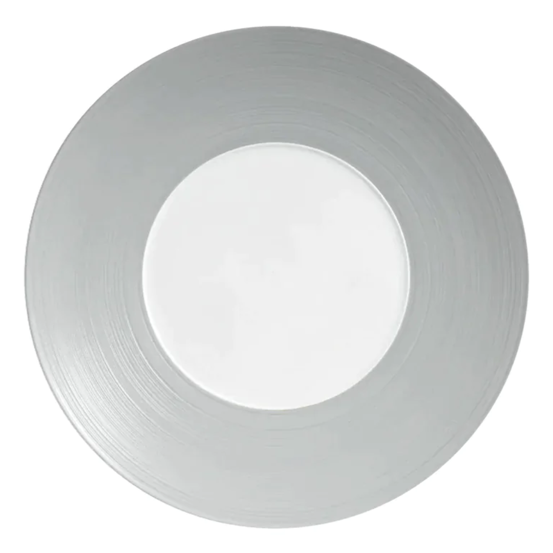 A silver charger plate by JL Coquet, featuring a brushed finish and a white Limoges porcelain center, inspired by the Hemisphere Dinnerware Grey collection.