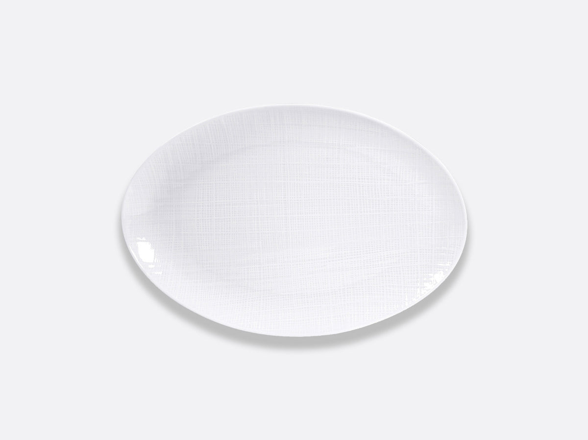 The Bernardaud Organza White Dinnerware features an elegant, oval porcelain plate with a subtle textured pattern on a light gray background—ideal for minimalist interior décor.