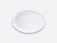 The Bernardaud Organza White Dinnerware features an elegant, oval porcelain plate with a subtle textured pattern on a light gray background—ideal for minimalist interior décor.