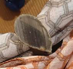 A close-up of scorched fabric and an iron’s soleplate contrasts with an elegant table set with Iza Silva’s Gemstone Napkin Ring Set of 4 - Grey, featuring geometric gray and orange patterns on the damaged napkin.