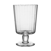 The Lando Pleat Glassware by MATCH features a tall, clear, mouth-blown glass with vertical ridges, a flared rim, and a footed base, inspired by antique Italian designs.