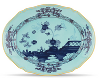 The Oriente Italiano Dinnerware Iris by Ginori 1735 is an oval Italian porcelain plate with a scalloped edge, featuring chinoiserie floral and landscape patterns in blue with gold accents on a light blue background.