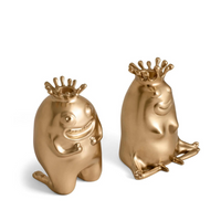 The Haas King & Queen Candlesticks by L'Objet feature whimsical, golden figurines with crowns—one kneeling and smiling, the other sitting cross-legged with closed eyes. Perfect playful luxury collectibles, ideal as a gift.