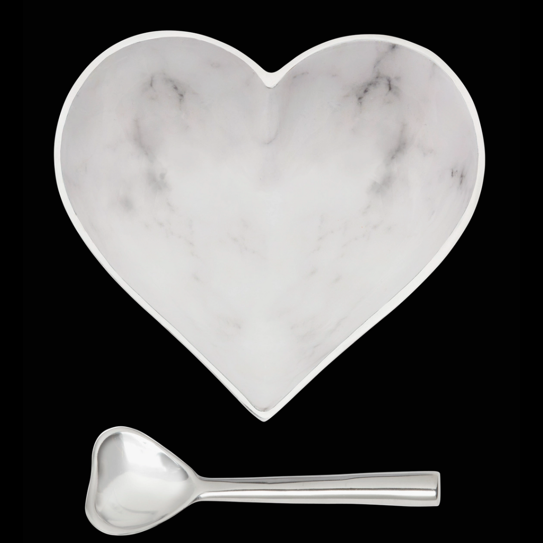 The Inspired Generations Happy Heart Bowl With Spoon in White Marble, featuring subtle gray veining and a shiny metallic rim and handle, is shown against a black background. Both handcrafted pieces are part of the Happy Heart Bowls collection.