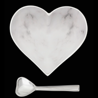 The Inspired Generations Happy Heart Bowl With Spoon in White Marble, featuring subtle gray veining and a shiny metallic rim and handle, is shown against a black background. Both handcrafted pieces are part of the Happy Heart Bowls collection.